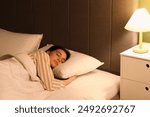 Young woman in pajamas sleeping on cozy bed in bedroom at night