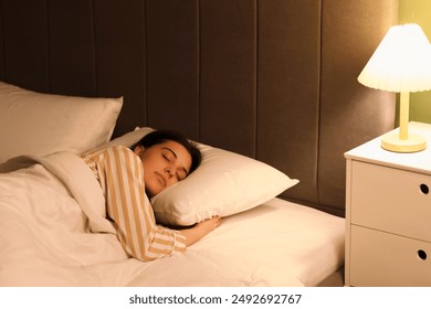 Young woman in pajamas sleeping on cozy bed in bedroom at night