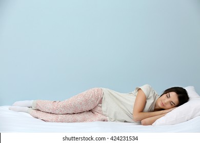 Young woman in pajamas sleeping on bed on blue background