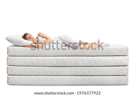 Young woman in pajamas sleeping on pile of mattresses isolated on white background