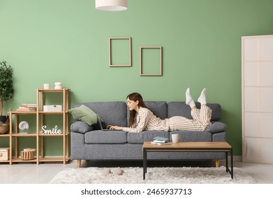 Young woman in pajamas working with laptop and lying on sofa at home. Remote work concept - Powered by Shutterstock