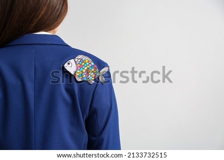 Young woman with paper fish attached to her back on grey background. April fools day celebration