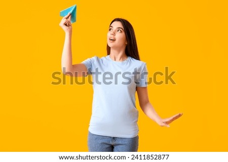Young woman with paper plane on yellow background