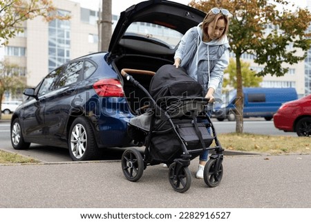 young woman parent folds the baby stroller into the luggage compartment of the car