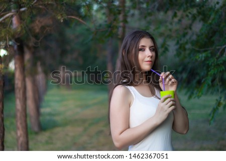 Young woman in a park drinking a refreshing drink from a plastic cup