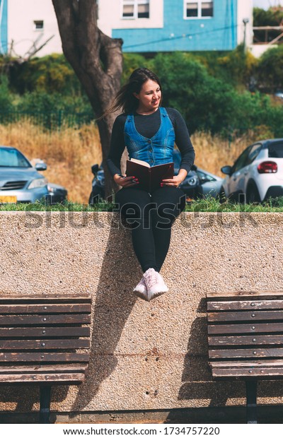 Young woman in park with notebook and pen on\
green background. Wish Marathon. Writing dreams and wishes in a\
notebook. Life with a clean slate. Planning a new week. Life after\
quarantine epidemic