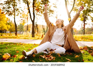 Young woman in park on sunny autumn day, smiling, having fun with leaves. Autumn fashion. Lifestyle. Relax, nature concept. 