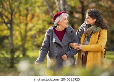 Young woman in park wearing winter clothing walking with old grandmother. Smiling lovely caregiver and senior lady walking in park during autumn and looking at each other with copy space.  - Shutterstock ID 2040685925