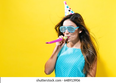 Young woman with party hat with noisemaker on a yellow background