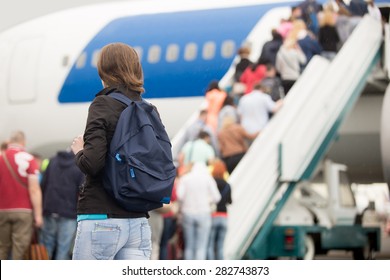 Young woman passenger in 20s travelling with backpack, boarding airplane, people climbing ramp on background, rear view