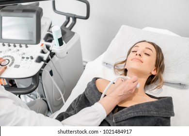 Young woman patient during the ultrasound examination of a thyroid lying on the couch in medical office - Powered by Shutterstock