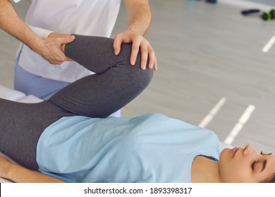 Young woman patient lying and getting procedure of knee and leg joints from chiropractor during visit at rehabilitation theapy in manual therapy clinic. Osteopath during work