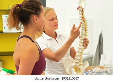 Young woman patient at physiotherapy consultation, physiotherapist explaining back bones on spine model