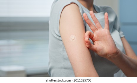Young Woman Patient Shows OK Gesture With Fingers Near Small Injection Spot On Forearm Skin Sitting In Hospital Room Close View