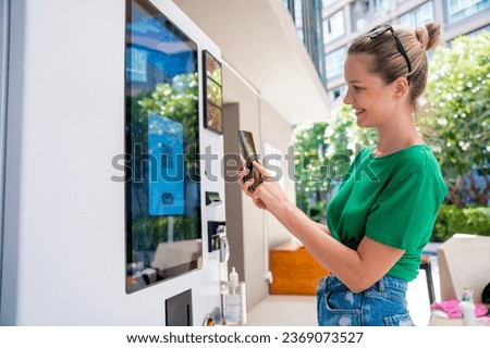 Young woman paying for coffee at vending machine using contactless method of payment 