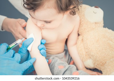 Young woman pediatrician performs a vaccination of a little girl. The girl is holding a mascot.