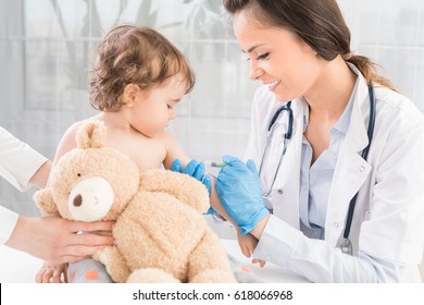 Young woman pediatrician performs a vaccination of a little girl. The girl is holding a mascot.