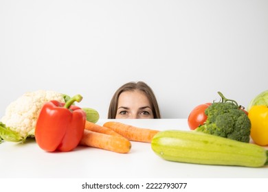 Young Woman Peeking Out From Under The Table Looking At Fresh Vegetables.