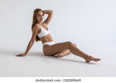 Young Woman With Perfect Body In Underwear Sitting On Floor Posing On White Studio Background. Body Care, Female Beauty, Spa Concept