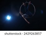 Young woman performing acrobatic element on aerial ring against dark background. Space for text