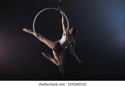 Young woman performing acrobatic element on aerial ring indoors - Powered by Shutterstock