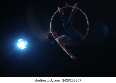 Young woman performing acrobatic element on aerial ring against dark background. Space for text - Powered by Shutterstock