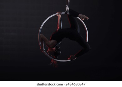 Young woman performing acrobatic element on aerial ring against dark background - Powered by Shutterstock