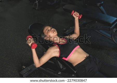 A young woman performing dumbbell chest flyes on an incline bench. Training upper body at the gym.