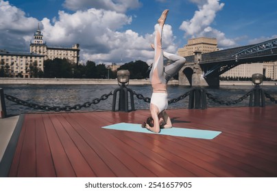 Young woman performing a forearm stand on a yoga mat by the river, showcasing balance, strength, and concentration. Background features an urban bridge, blue sky, modern architecture,creating serene - Powered by Shutterstock