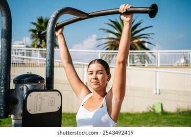 Young woman performing pull-ups on outdoor gym equipment in urban park setting - Powered by Shutterstock