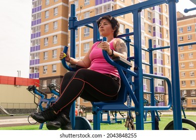 young woman performs exercises outdoor using street fitness combo machine - Powered by Shutterstock