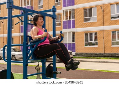 young woman performs exercises outdoors using street fitness combo machine - Powered by Shutterstock