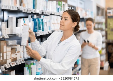 Young woman pharmacist in uniform arranges products on shelves in pharmacy - Powered by Shutterstock