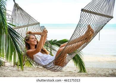 Young Woman With Phone In The Hammock On A Tropical Beach
