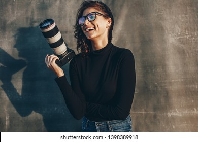 Young woman photographer with her professional camera smiling against oliphant backdrops. Woman photographer with digital camera. - Powered by Shutterstock