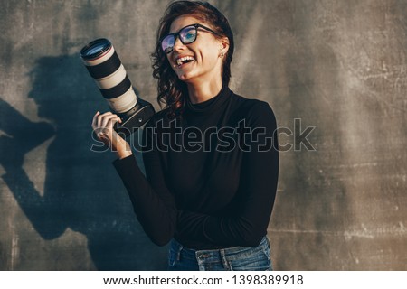 Young woman photographer with her professional camera smiling against oliphant backdrops. Woman photographer with digital camera.