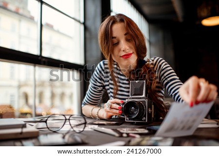 Young woman photographer looking at the printed photos with old 6x6 frame camera sitting in the cafe with loft design interior