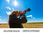 Young woman photographer with telephoto lens attached to DSLR camera shooting towards the sky i a bright sunny day. Copy space on top, lens flares