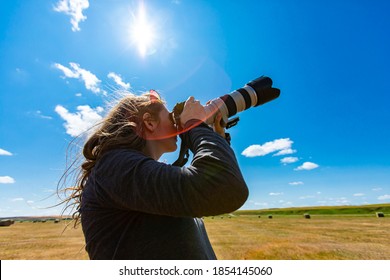 Young woman photographer with telephoto lens attached to DSLR camera shooting towards the sky i a bright sunny day. Copy space on top, lens flares