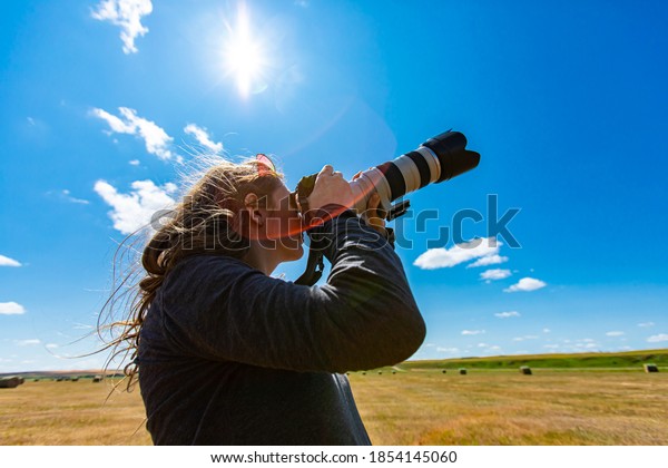 Young woman photographer with telephoto lens\
attached to DSLR camera shooting towards the sky i a bright sunny\
day. Copy space on top, lens\
flares