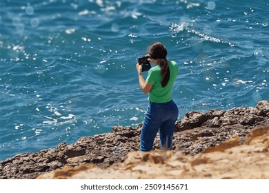 Young woman photographing the sea with a camera on a rocky shore - Powered by Shutterstock