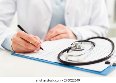 Young woman physician with stethoscope prescribing treatment to patient. Female doctor with pen writing recipe on clipboard in hospital. 
