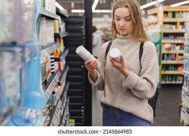 Young Woman Picking Bottles With Shampoo And Conditioner From Shelf In Cosmetics Store