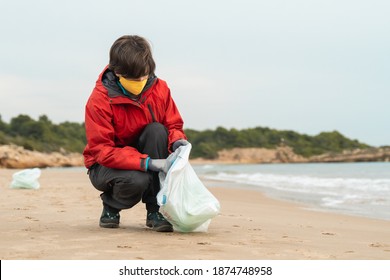 Young woman picking up disposable medical mask and gloves from beach - Environmental and ocean pollution during Coronavirus outbreak - Powered by Shutterstock