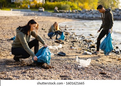 Young woman picking up garbage in bag at beach - Powered by Shutterstock