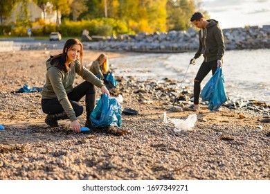 Young Woman Picking Up Garbage In Bag At Beach