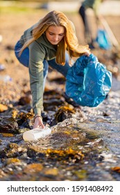 Young Woman Picking Up Garbage From Rocky Shore