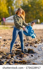 Young Woman Picking Up Garbage From Rocky Shore