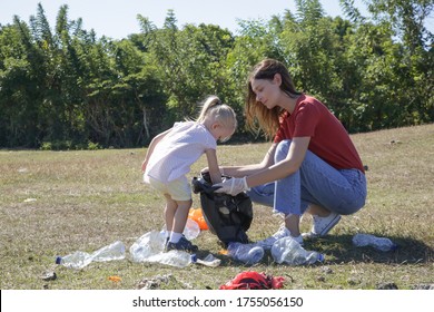 Young woman picking up plastic waste from the meadow with her toddler girl. Collecting garbage is educational activity to involve children in the protection of the environment.