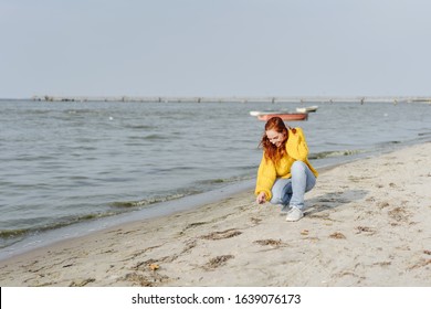 Young Woman Picking Up Shells On A Beach Kneeling On The Sand At The High Tide Line On A Winter Day